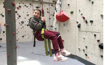 Ein Kind gesichert an Seilen. Es ist ist in einer Kletterhalle.